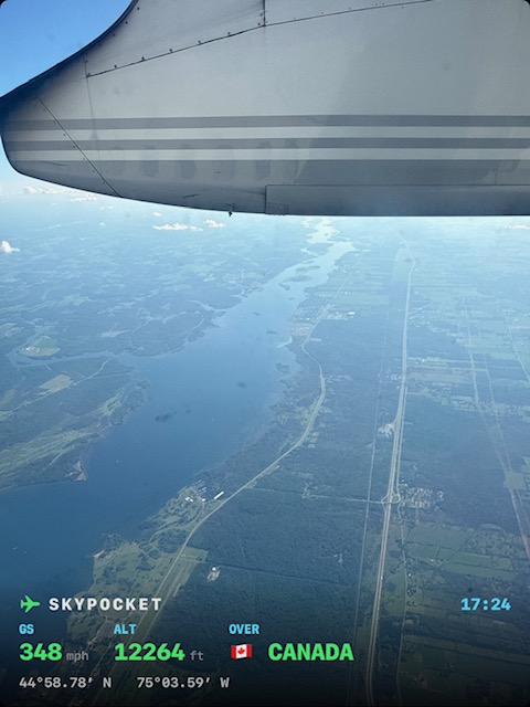 Real photo from the window seat: the wing over the St. Lawrence as the stamp flips to Canada, 348 mph at 12,264 ft